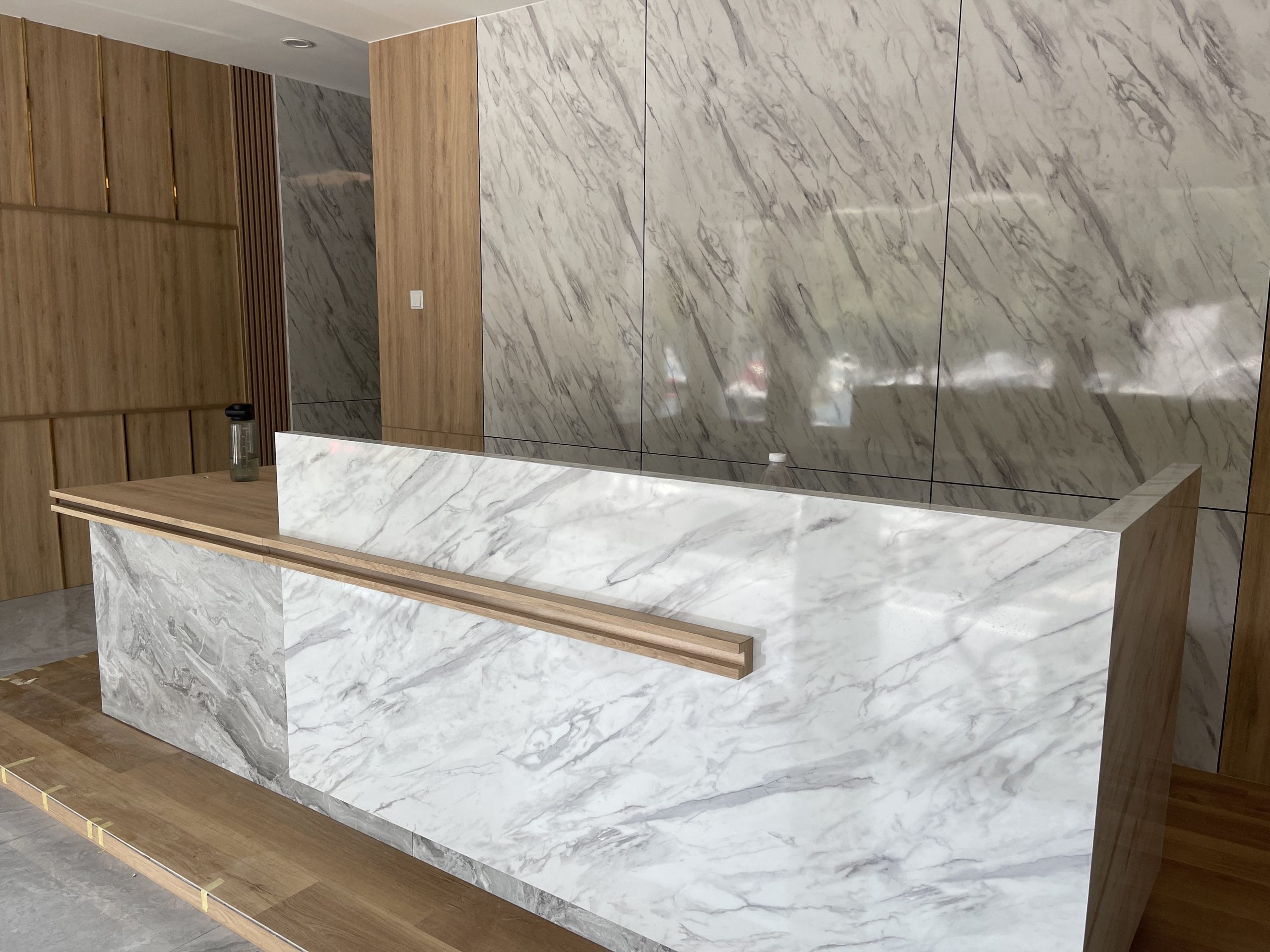 Built-in reception counter clad in white marble with a timber handrail detail, set against a matching marble and timber feature wall.