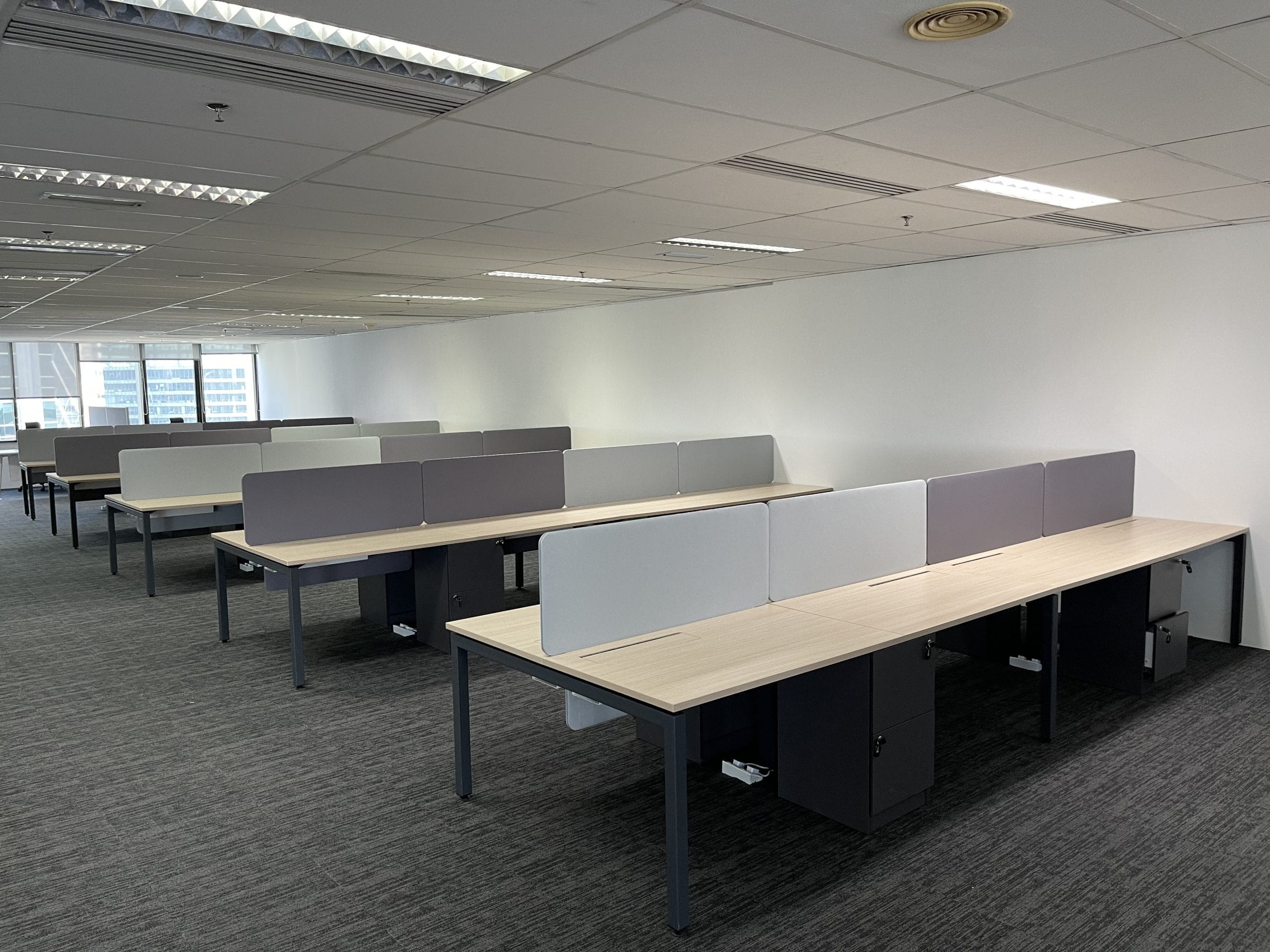 Long rows of bench desks with grey fabric screens running down the spine of each row, the ends of every run left open to the floor.
