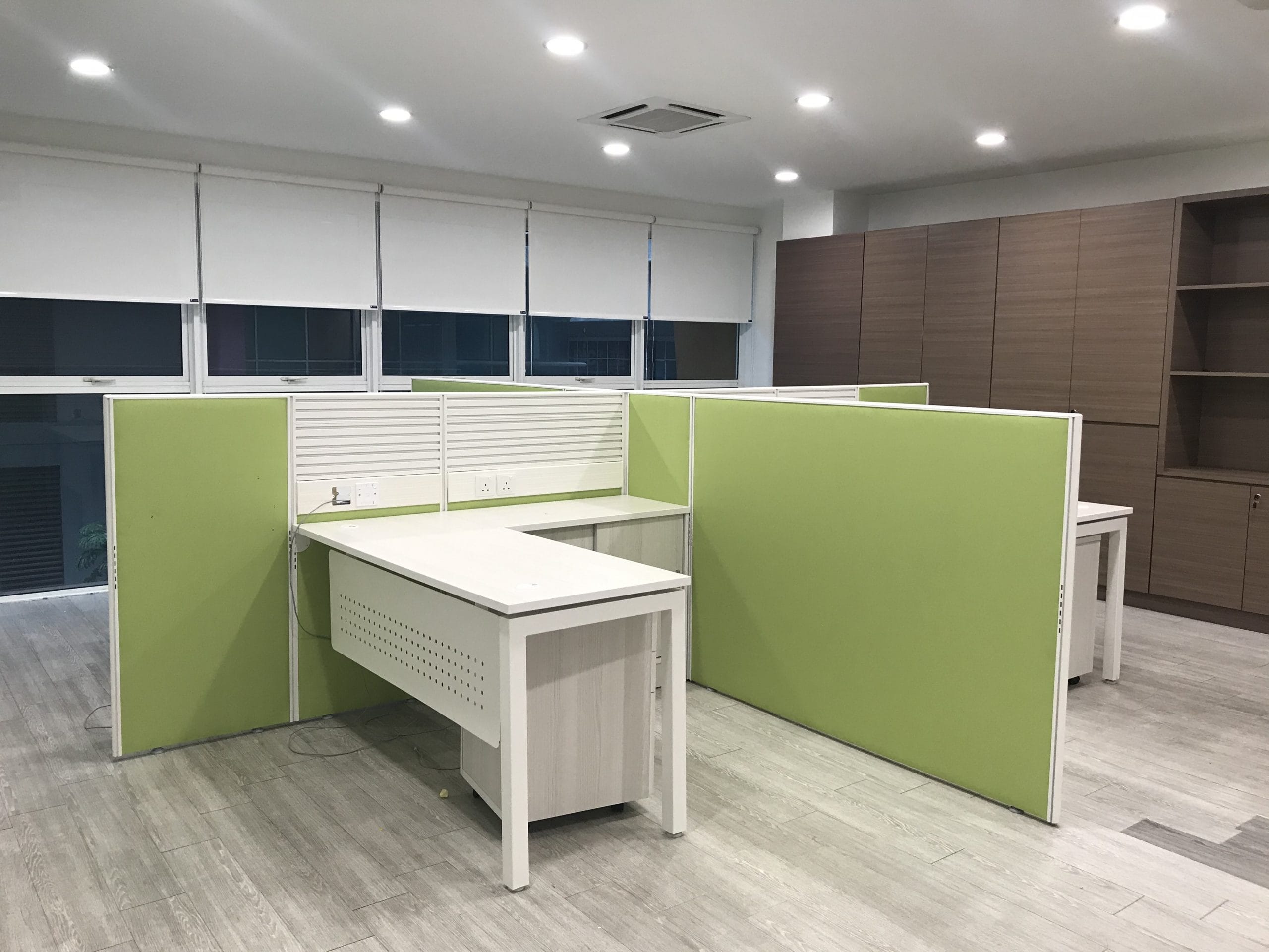 Green fabric partition panels enclosing L-shaped desks, the outer panels carried well above seated head height while the lower slatted sections between the desks stop just above the worksurface.